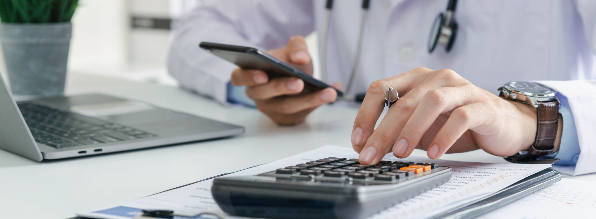 A healthcare provider using a calculator and smartphone while analyzing revenue cycle analytics data on a practice management dashboard.